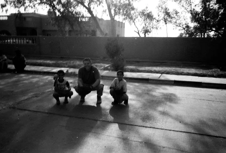 Craig Smith crouching in a street with young Iraqi children, Najaf, Iraq