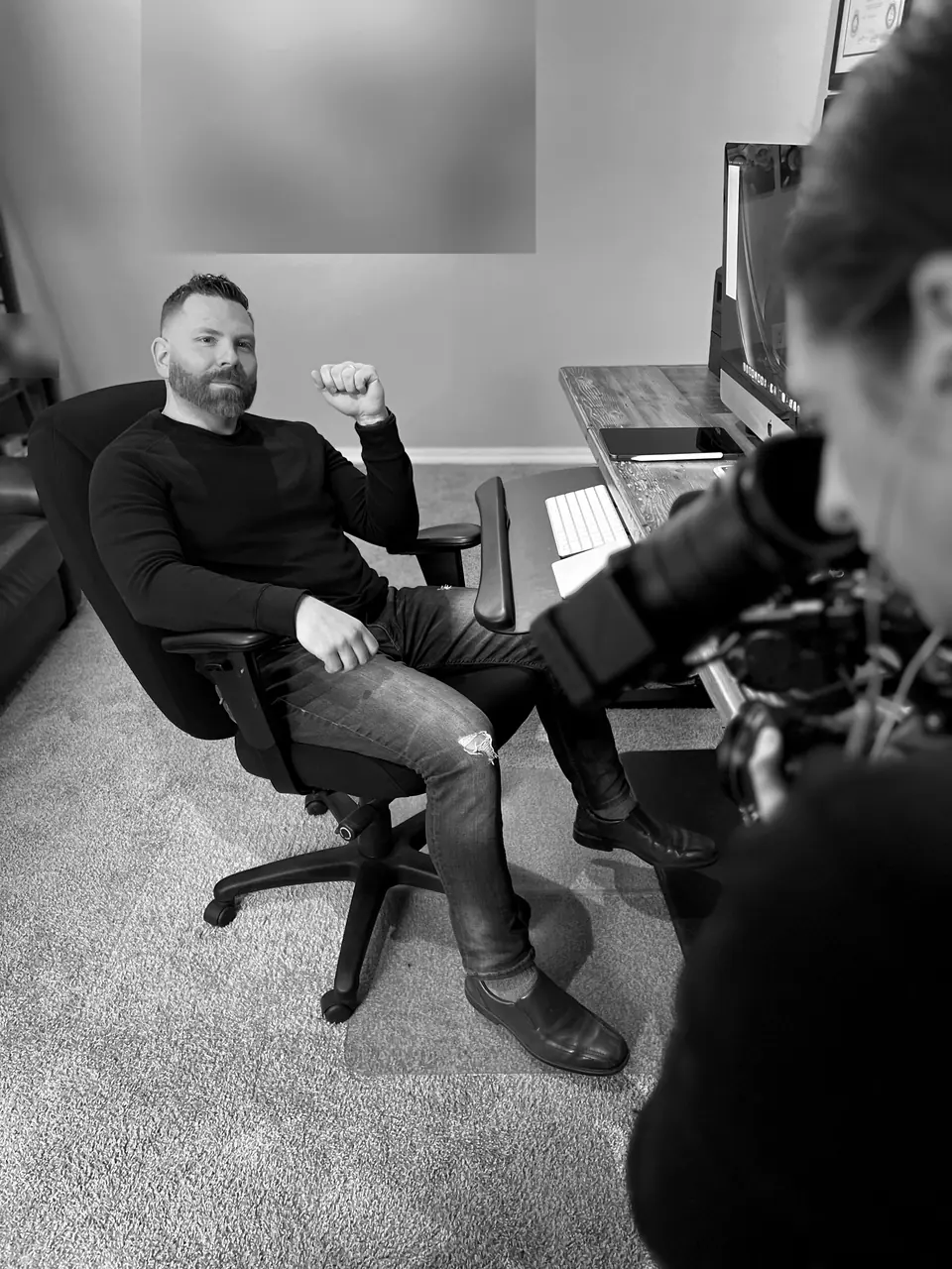 Behind the scenes filming for A&E’s Accused: Guilty or Innocent? (John Lott case): Craig Smith seated in an office chair facing the camera; family photos on the wall obscured