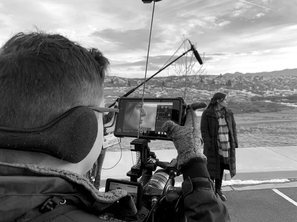 A camera operator filming a woman outdoors at dusk